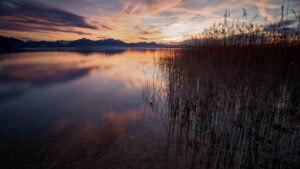 Rosa-oranger Schimmer in den Wolken, der sich auf dem See widerspiegelt. Langzeitbelichtung mit 50 Sekunden.